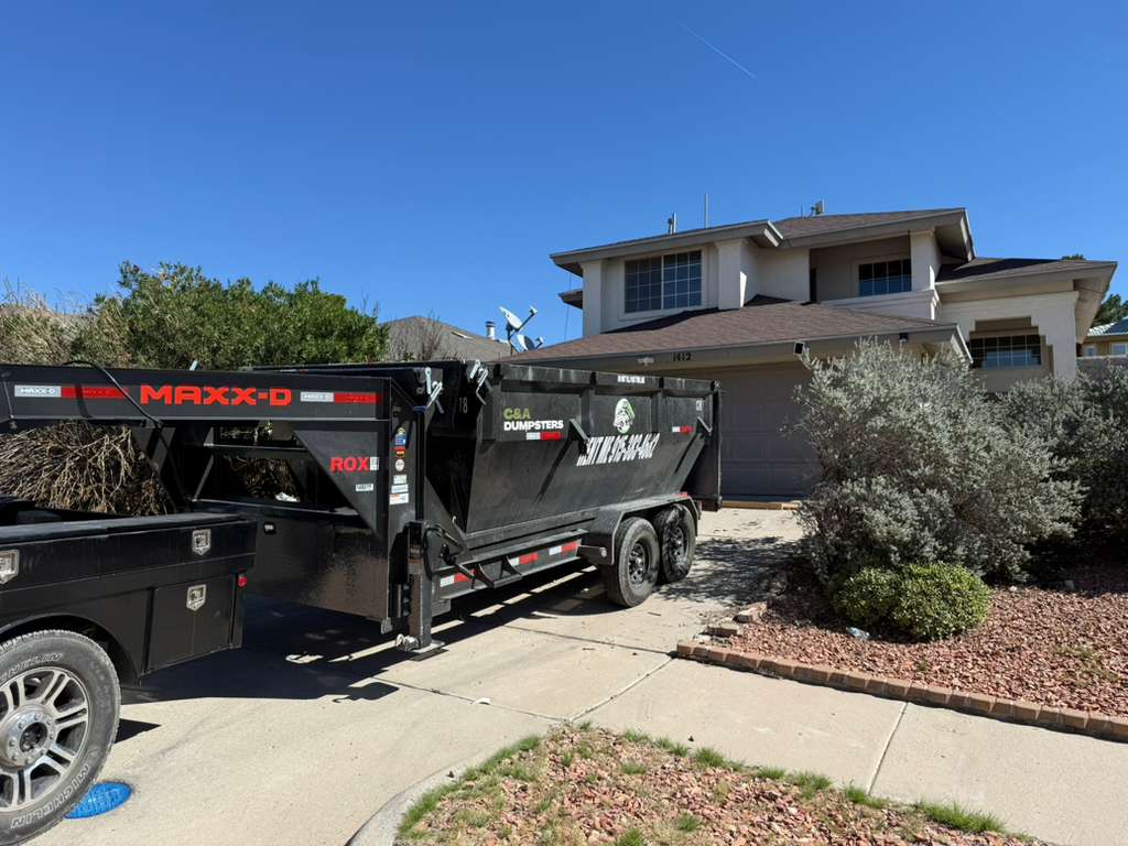Dumpster on driveway loaded with yard waste and landscaping debris